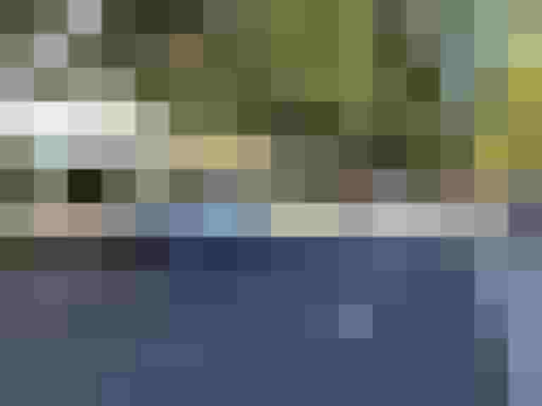 Straße mit Fahrzeugen und Passanten, umgeben von Bäumen und Gebäuden.