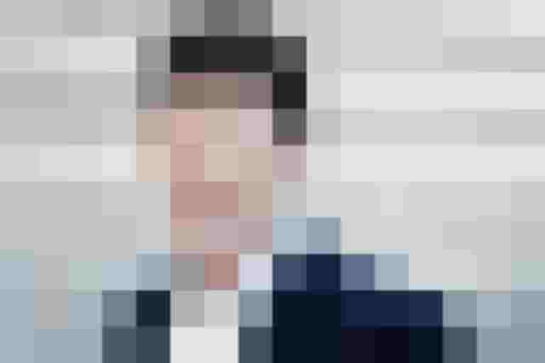 Mann in Anzug lächelt vor grauer Hintergrundwand, Thema: Klimaschutz & Mobilität.