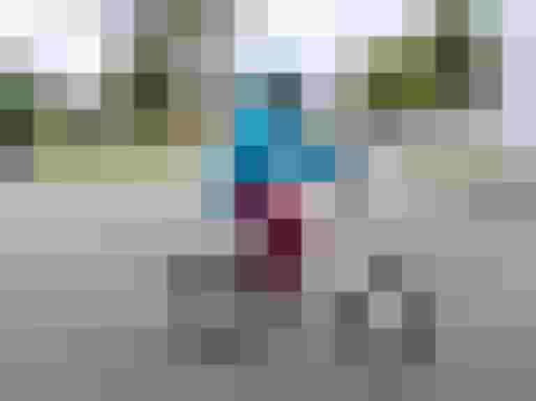 Frau in blauer Kleidung fährt E-Bike auf Asphaltstraße, Hintergrund mit Bäumen und Gebäuden.