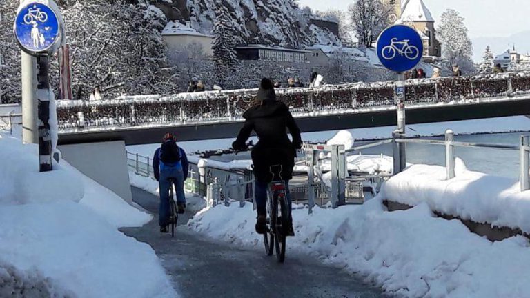 Winterliche Radfahrer auf einem verschneiten Fahrradweg in Salzburg.