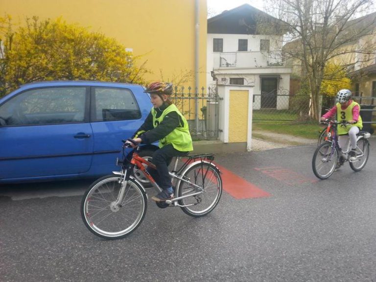 Kinder in Sicherheitswesten fahren Rad auf einer Straße, Förderung des Radverkehrs in Salzburg.