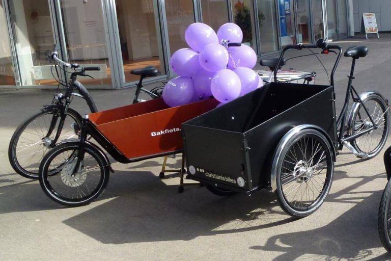 Zwei Lastenfahrräder mit lila Ballons vor einem Gebäude in Anif.