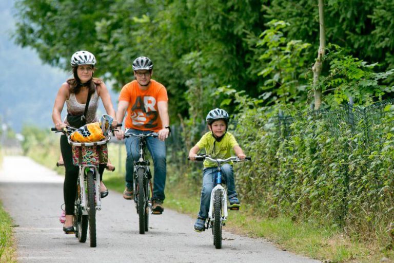 Familie fährt gemeinsam mit Fahrrädern auf einem Schotterweg in der Natur.