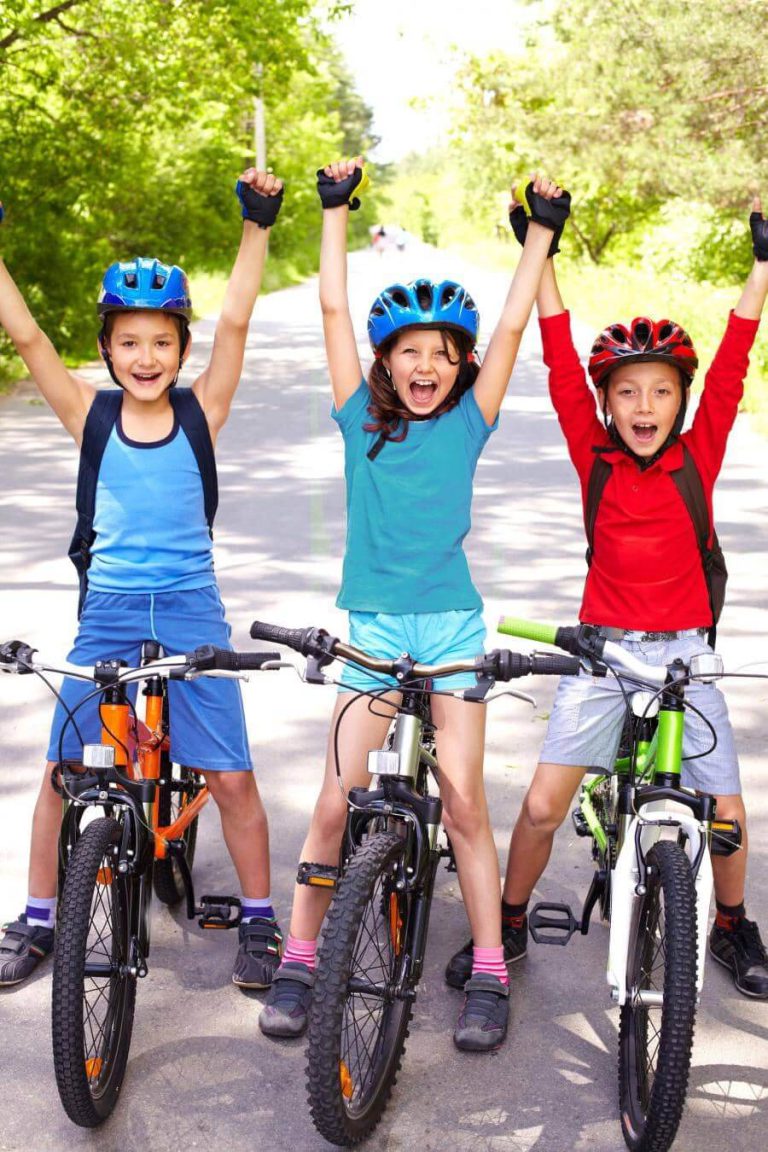 Drei Kinder mit Fahrrädern jubeln auf einer Straße umgeben von Bäumen, inspiriert zum Radfahren.