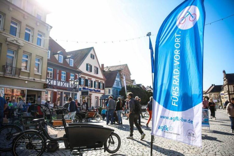 Bunte Straßenveranstaltung mit Cargobikes und Menschen vor historischen Gebäuden.