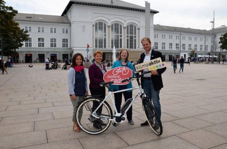 Gewinner mit E-Bike und Schildern von „Salzburg radelt“ und „klimaaktiv“ in der Stadt.
