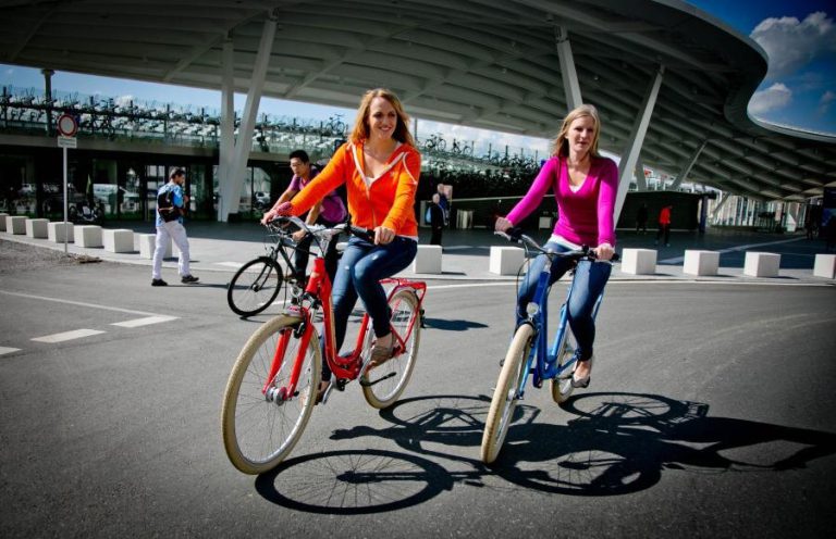 Zwei Frauen fahren fröhlich mit Fahrrädern auf einer Straße in Salzburg.