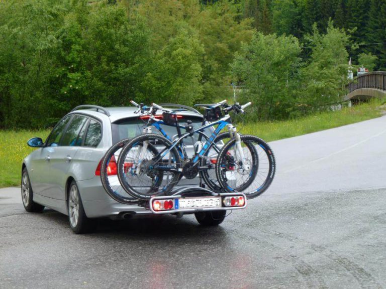 Fahrradheckträger mit drei Fahrrädern auf einem Auto vor grüner Natur.