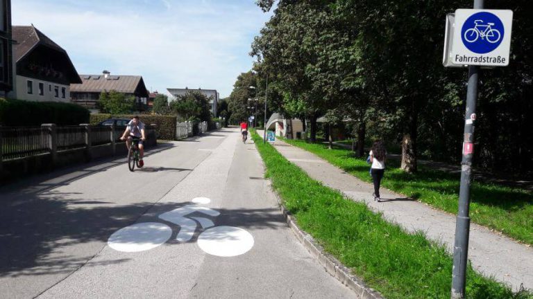 Neue Fahrradstraße in Salzburg mit Radfahrern und Fußweg unter Bäumen.