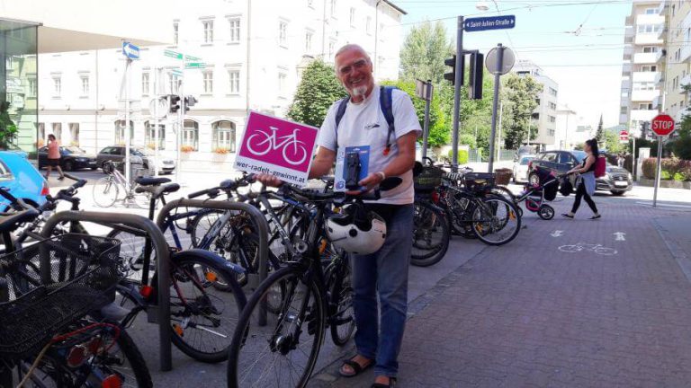 Glücklicher Gewinner hält Preis an Fahrrad, umgeben von anderen Fahrrädern in Salzburg.