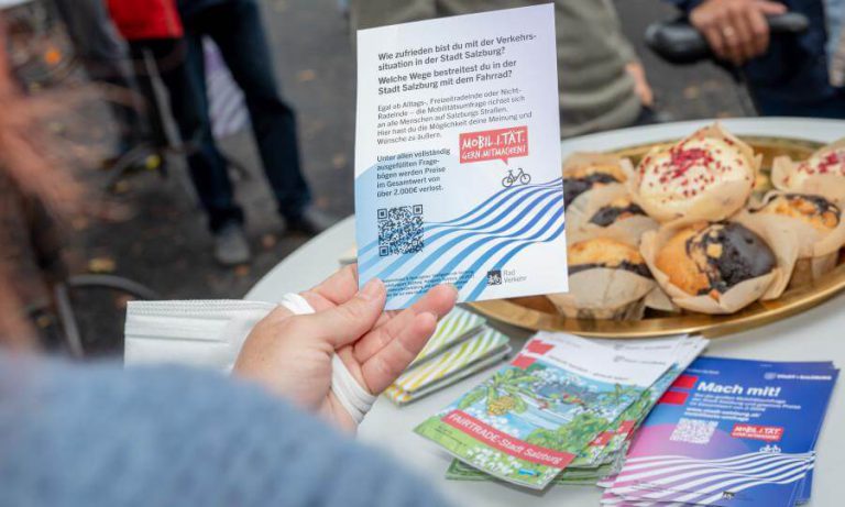 Hand mit Umfrageauftrag zur Rad-Mobilität in Salzburg, daneben stehen Muffins und Flyer.