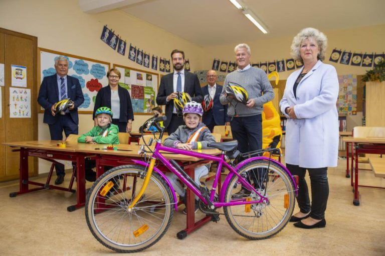 Gruppenszene mit Kindern und Erwachsenen, die Radhelme für die Aktion „Sicheres Köpfchen“ halten.