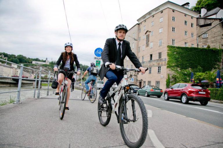 Radfahrer in Anzug und Freizeitkleidung auf Stadtroute in Salzburg, symbolisieren nachhaltige Mobilität.