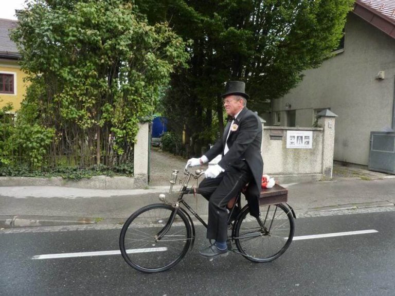Mann im Zylinder fährt auf historischem Fahrrad in urbaner Umgebung.