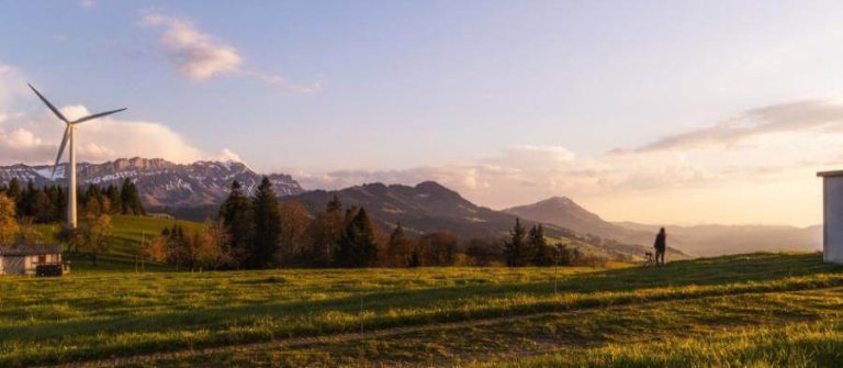 Landschaft mit Windrad und Wanderer, umgeben von Bergen und Wiesen in Salzburg.