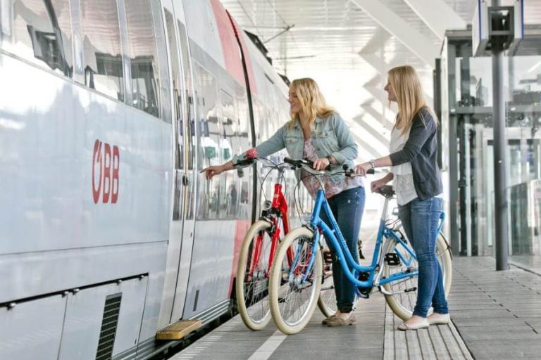 Zwei Frauen mit Fahrrädern an einem Bahnhof, bereit zur kostenlosen Mitnahme im Zug.