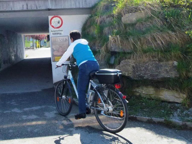Seniorin fährt mit E-Bike durch einen Tunnel; Verkehrssicherheit und Mobilität im Fokus.