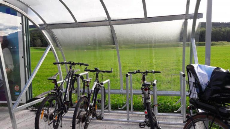 Überdachte Radabstellanlagen an einer Haltestelle in einer ländlichen Umgebung.