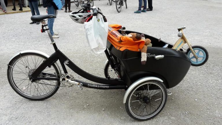 Lastenrad mit Spielzeug und Einkaufstasche auf einem Platz, symbolisiert nachhaltige Mobilität.