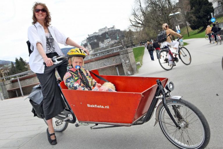Frau mit Kind auf einem Lastenrad in einer urbanen Umgebung in Salzburg.
