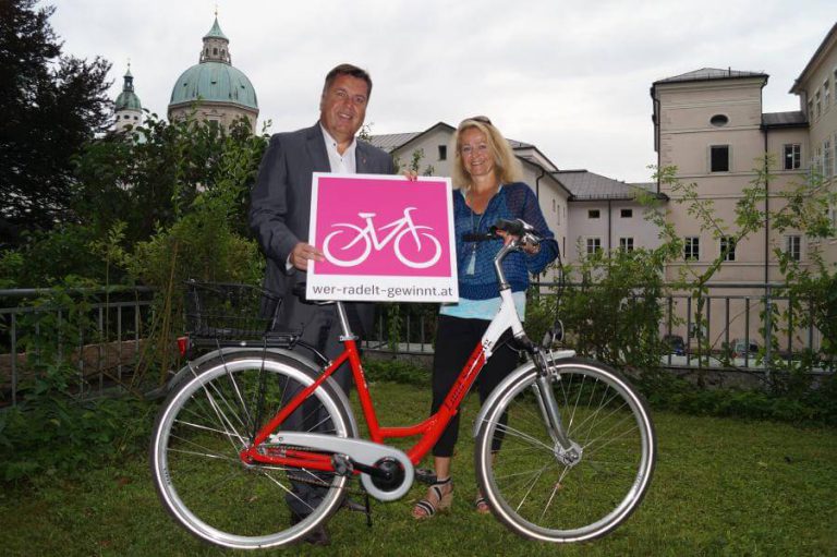 Doris Racker-Weidinger mit Preisgutschein und Fahrrad im Salzburger Stadtbild.