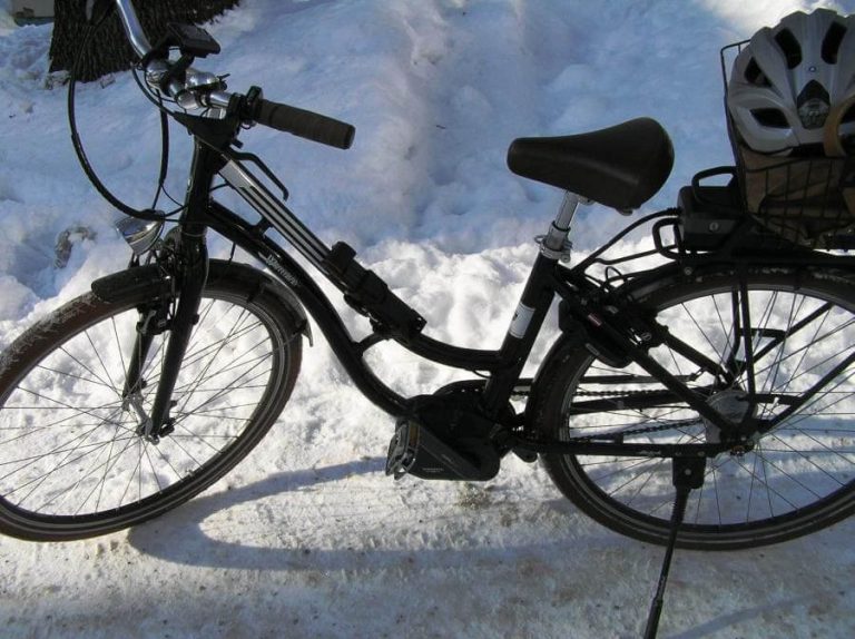 E-Bike steht auf Schnee, Helm und Gepäckträger sind sichtbar, ideal für Winterradeln.