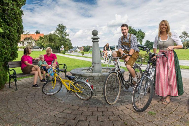 Familientag am Obertrumer See: Radfahrer und Kinder am Brunnen, Spaß und Gesellschaft im Freien.