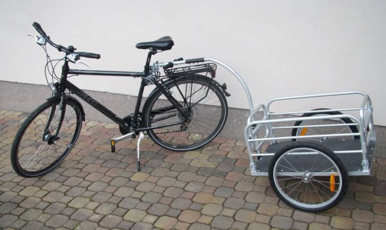 Schwarzes Fahrrad mit silbernem Lastenanhänger auf Pflasterboden.