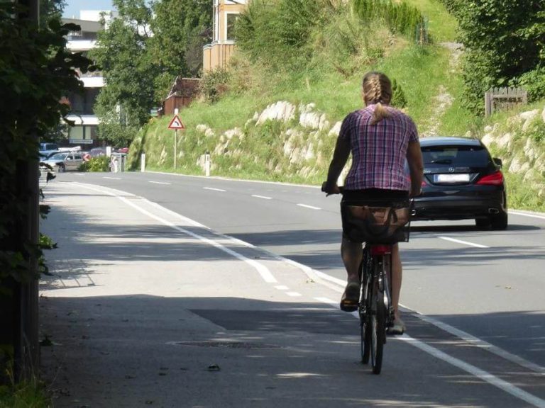 Frau mit Zopf radelt auf Radweg in städtischer Umgebung an Straße entlang.