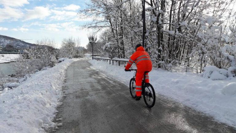 Radfahrer in warmer Kleidung auf verschneiter Straße, umgeben von winterlicher Landschaft.