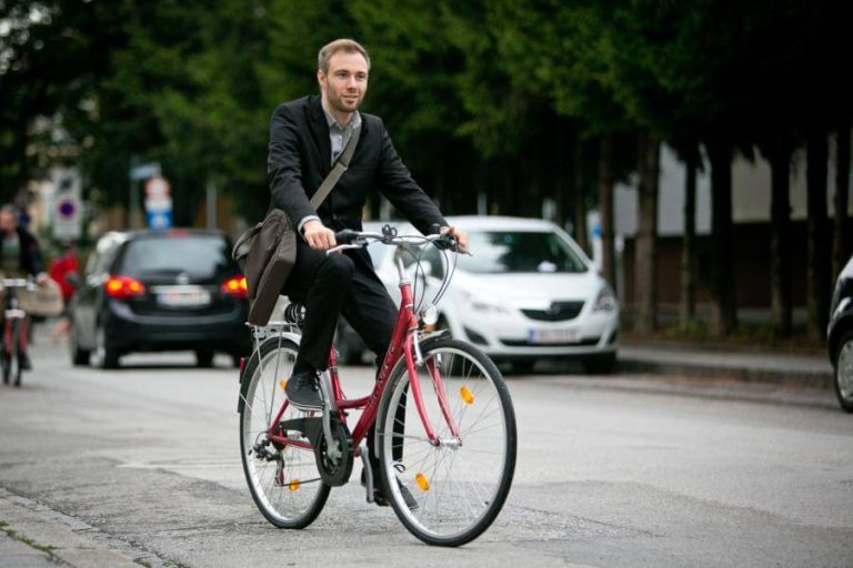 Mann im Anzug radelt entspannt auf einer Straße mit Autos, fördert nachhaltige Mobilität.