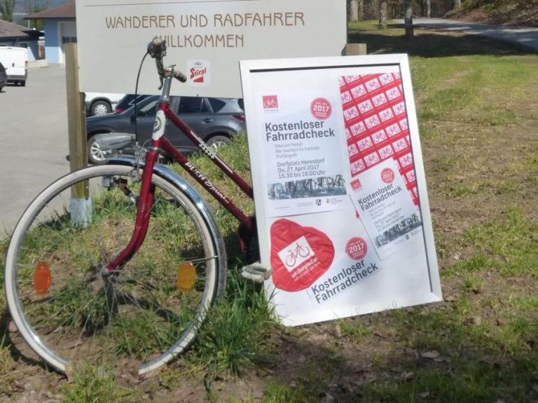 Rotes Fahrrad neben Schild für kostenlosen Fahrradcheck in Salzburg.