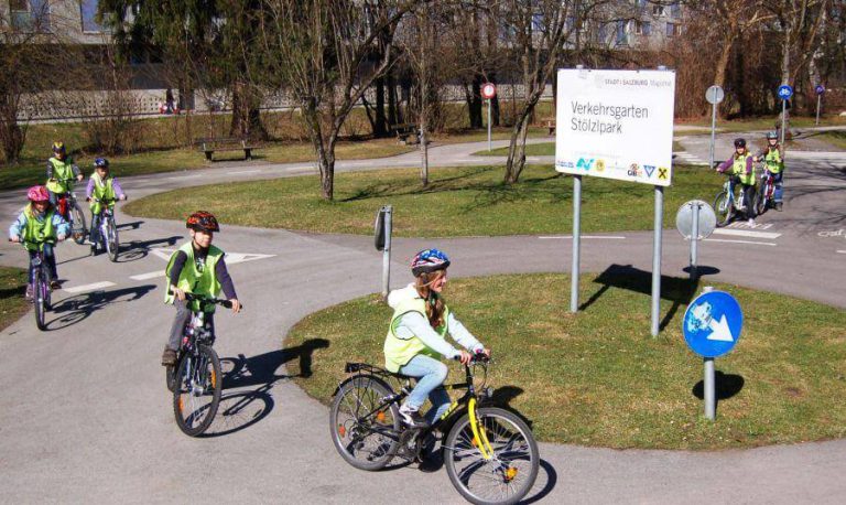 Kinder in Leuchtwesten üben Radfahren im Verkehrsgarten Stölzlpark in Salzburg.
