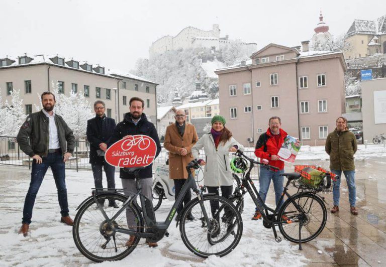 Teilnehmer von „Salzburg radelt“ posieren vor schneebedeckter Kulisse mit Fahrrädern.