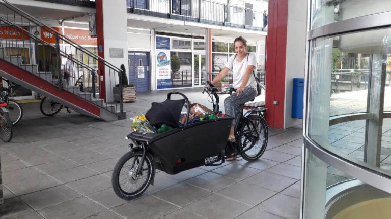 Frau auf einem Lastenrad mit Einkäufen in einer urbanen Umgebung in Salzburg.