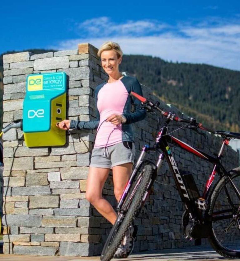 E-Bike-Ladestation am Tauernradweg mit Nutzerin und Mountainbike in der Natur.
