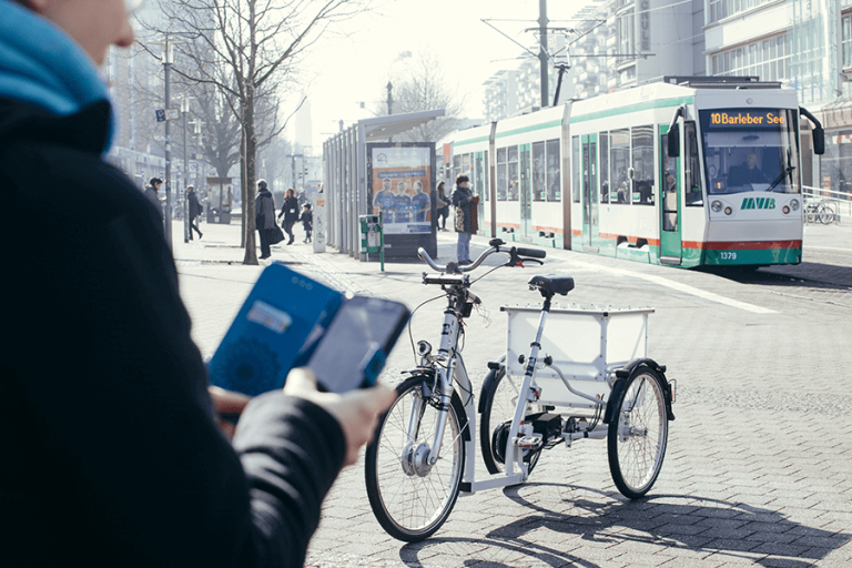 Autonomes E-Bike auf Straße, im Hintergrund Straßenbahn und Passanten, Fokus auf Mobilität.