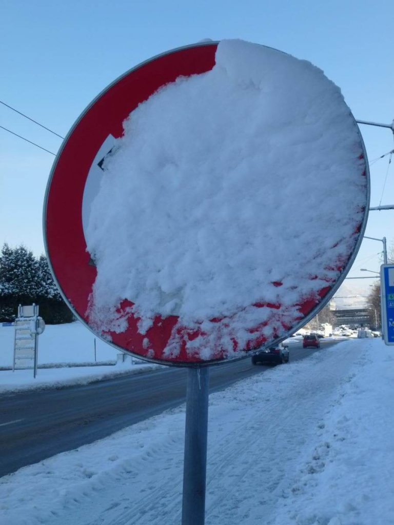 Verschneites Verkehrszeichen an einer Straße, Fahrregeln im Schnee unklar.