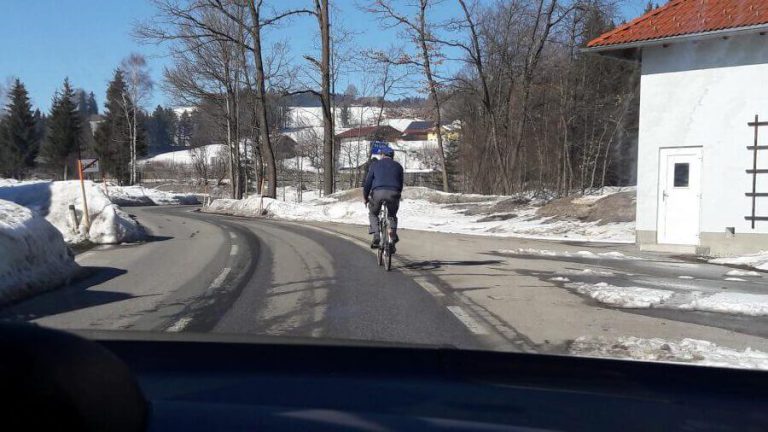 Radfahrer auf einer schneebedeckten Straße in winterlicher Landschaft bei klarem Himmel.