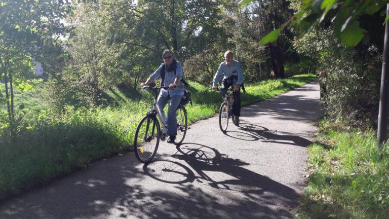 Zwei Radfahrer auf einem sonnigen Radweg, umgeben von grüner Natur in Salzburg.