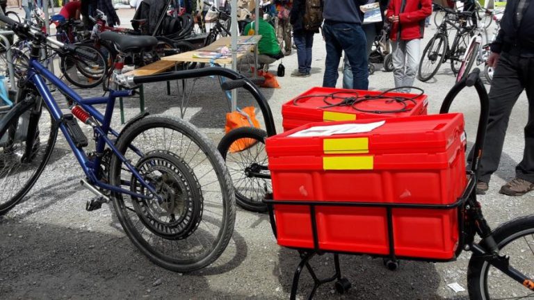 Zwei Fahrräder mit einem roten Lastenanhänger auf einer Veranstaltung in Salzburg.