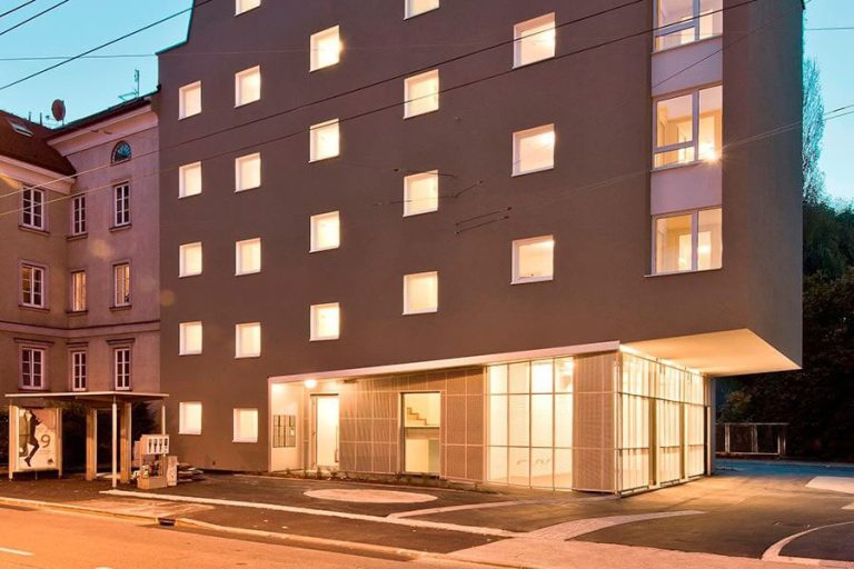 Moderne Gebäude mit leuchtenden Fenstern in Salzburg, ideal für nachhaltige Mobilität.