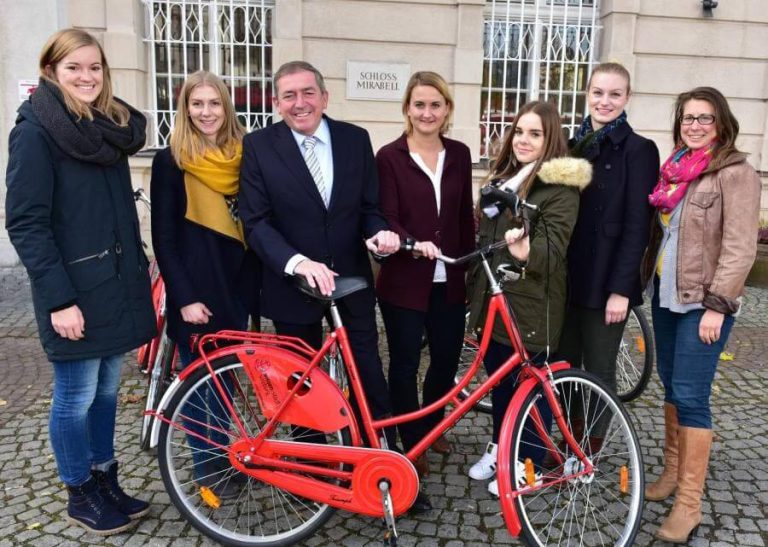 Fünf Studentinnen freuen sich mit einem roten Fahrrad beim Wissensstadt-Gewinnspiel in Salzburg.