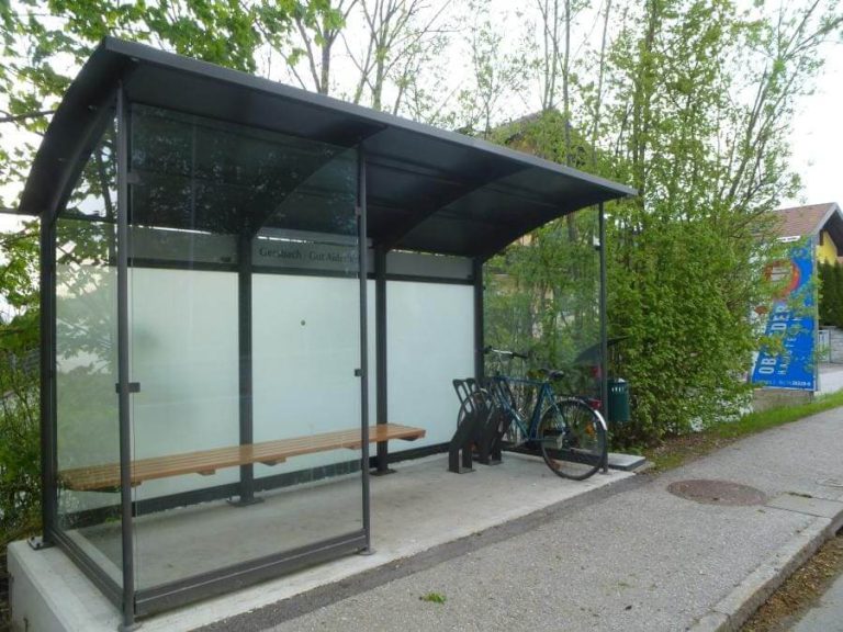 Moderne Bushaltestelle mit Fahrradabstellanlagen und Sitzgelegenheit in Naturumgebung.