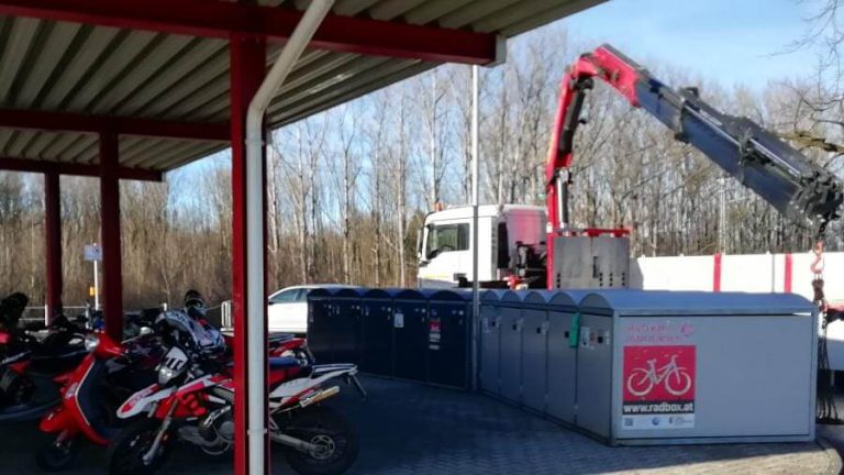 Rote Motorräder stehen vor neuen Radboxen an der Lokalbahn-Haltestelle Anthering.