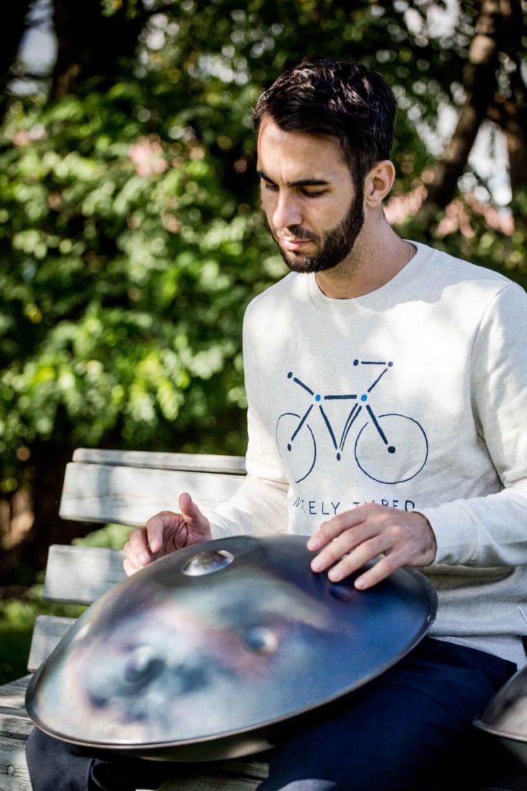 Mann spielt Hangdrum auf einer Parkbank, umgeben von grüner Natur. Radkultur und Musik vereint.
