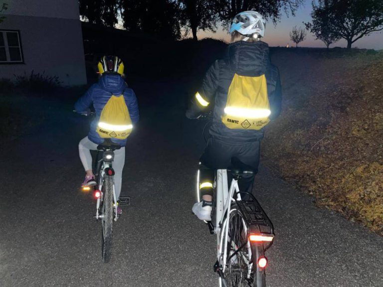 Radfahrende in reflektierenden Rucksäcken fahren bei Dämmerung auf einem Radweg.