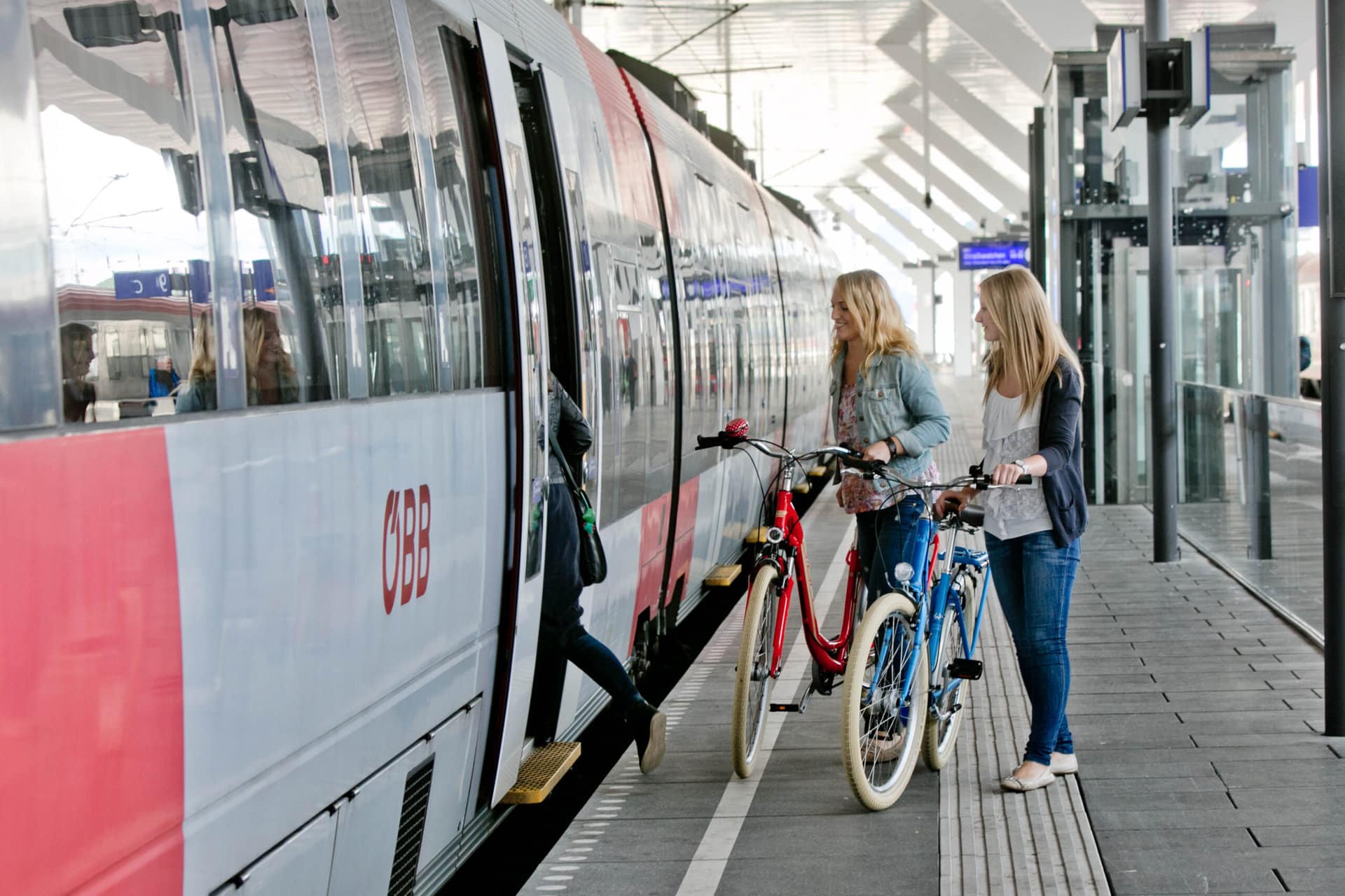 2 Frauen stehen mit 2 Fahrrädern am Bahnsteig vor einem Zug