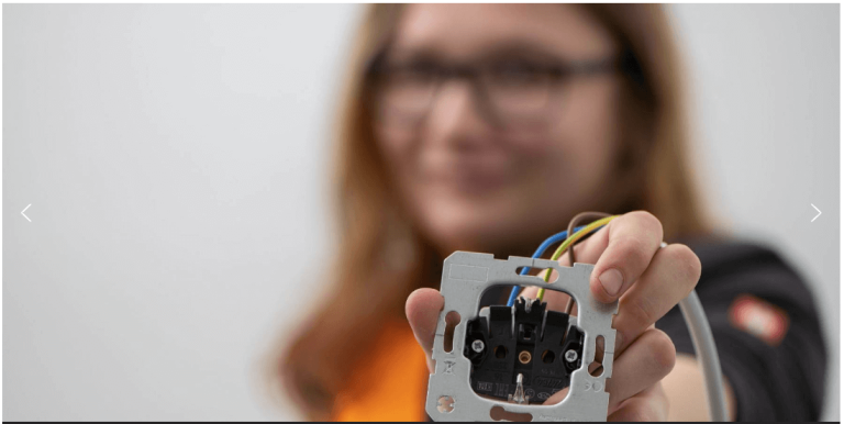 Frau hält eine Elektroinstallationseinheit mit farbigen Drähten in der Hand.