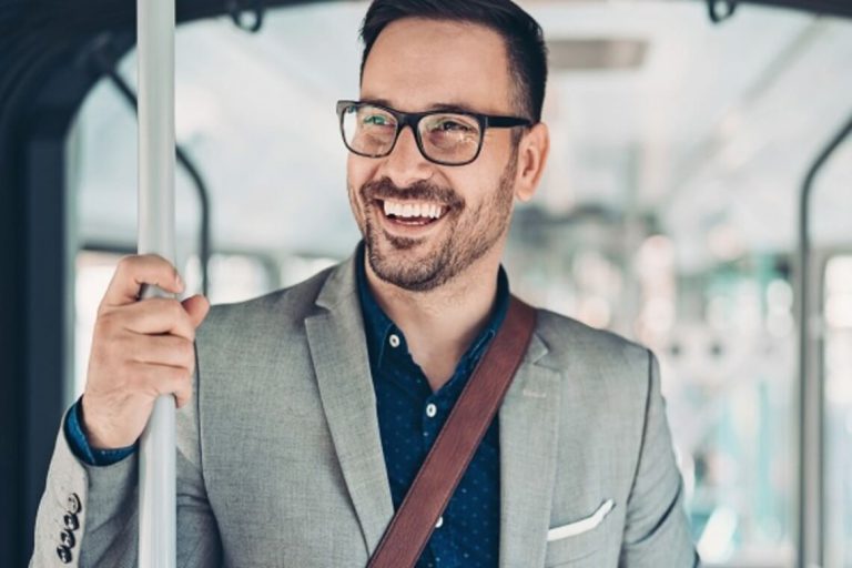 Mann im Anzug lächelt, während er sich in einem öffentlichen Verkehrsmittel festhält.